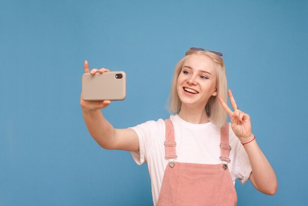 Mädchen in einer leichten Freizeitkleidung macht Selfie auf blauer Wand