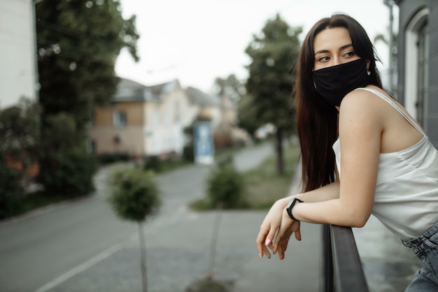 Mädchen in einer Schutzmaske auf einem Balkon betrachtet eine leere Stadt.