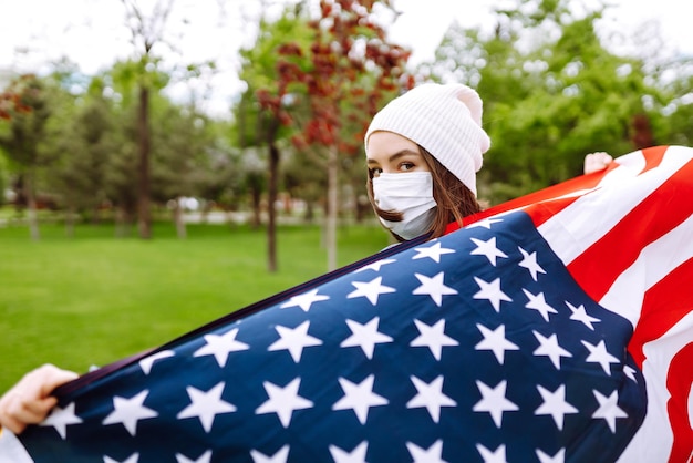 Mädchen in einer sterilen medizinischen Schutzmaske und mit amerikanischer Flagge in der Hand Quarantäne-Stadt Covid-19