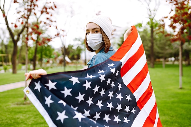 Mädchen in einer sterilen medizinischen Schutzmaske und mit amerikanischer Flagge in der Hand Quarantäne-Stadt Covid-19