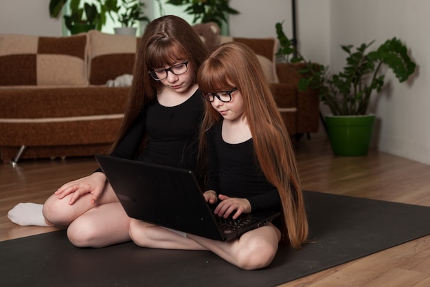 Mädchen in Fitness-Bodys sehen sich eine Online-Lektion auf einem Laptop an und dehnen sich.