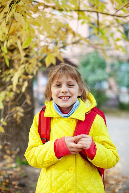 Mädchen in gelber Jacke und mit roter Aktentasche auf der Straße im Herbst