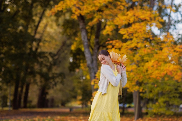 Mädchen in gelber Kleidung im Herbstpark freut sich im Herbst und hält gelbe Blätter in ihren Händen warm