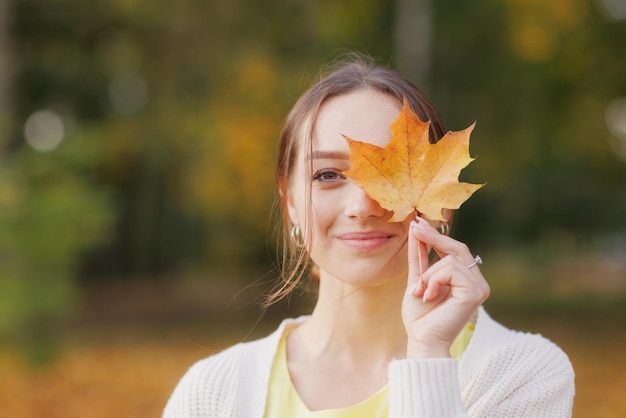 Mädchen in gelber Kleidung im Herbstpark freut sich im Herbst und hält gelbe Blätter in ihren Händen warm