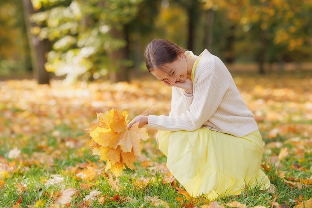 Mädchen in gelber Kleidung im Herbstpark freut sich über den Herbst und hält gelbe Blätter in ihren Händen. Warmes Herbstkonzept