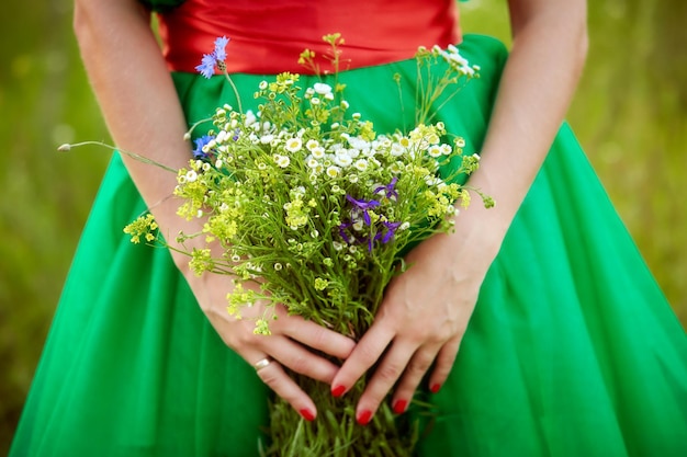 Mädchen in grünem Kleid mit roter Maniküre hält ein Feld wilder Blumenstrauß aus Sommerblumen Nahaufnahme Sommerzeit Sommerstimmungskonzept Hochwertiges Foto