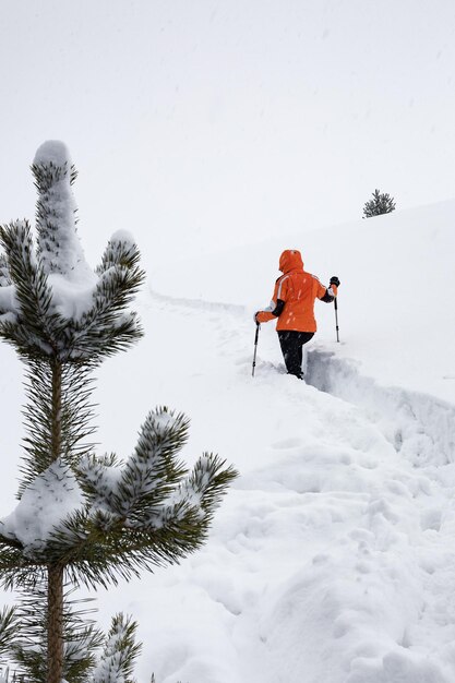 Mädchen in heller Jacke klettert den Berg entlang schmaler Pfade im Tiefschnee bei Schneefall