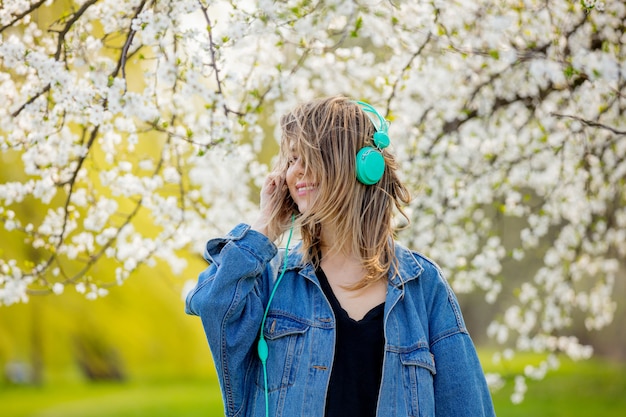 Mädchen in Jeansjacke und Kopfhörer steht in der Nähe eines blühenden Baumes