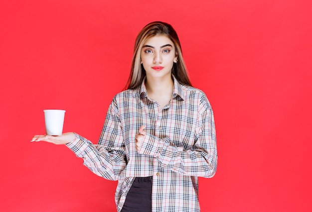 Mädchen in kariertem Hemd, das eine weiße Einweg-Kaffeetasse hält und den Geschmack genießt