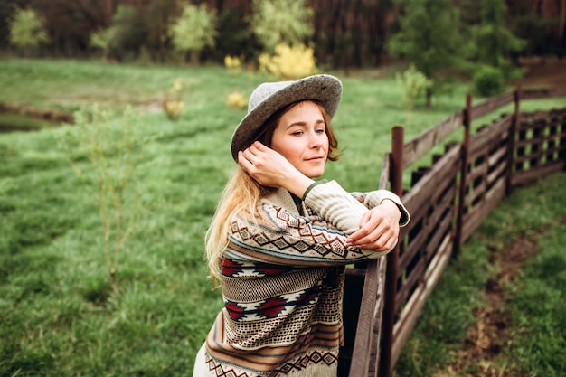 Mädchen in Kleidern mit ethnischen Mustern, die in Naturwand aufwerfen. Porträt der lächelnden jungen Frau im Boho-Hut. Nahaufnahmeporträt eines Mädchens in einem Hut an der Wand des Waldes in regnerischem Tag.