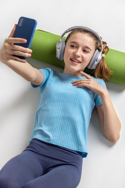 Mädchen in Kopfhörern mit Telefon ruht sich nach Yoga aus Grüne Teppichrolle unter deinem Kopf