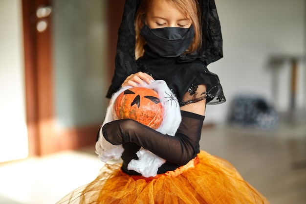 Mädchen in Maske zu Hause im Halloween-Kostüm mit Kürbis Jack oder Laurent