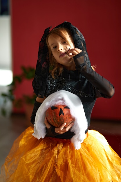 Foto mädchen in maske zu hause im halloween-kostüm mit kürbis jack oder laurent