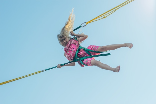 Foto mädchen in mehrfarbigem kleid fällt auf eine attraktion gegen den himmel.