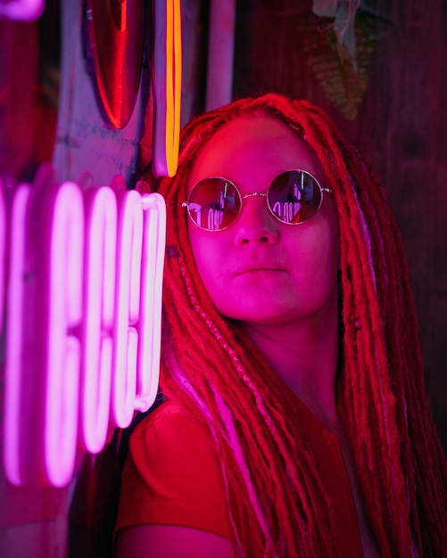 Mädchen in Neonlichtern, schöne Frau mit Sonnenbrille, mit rosa Haaren, mit Dreadlocks-Zöpfen,