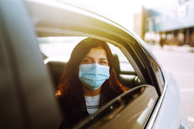 Mädchen in steriler medizinischer Schutzmaske auf ihrem Gesicht sitzt in einem Taxi.