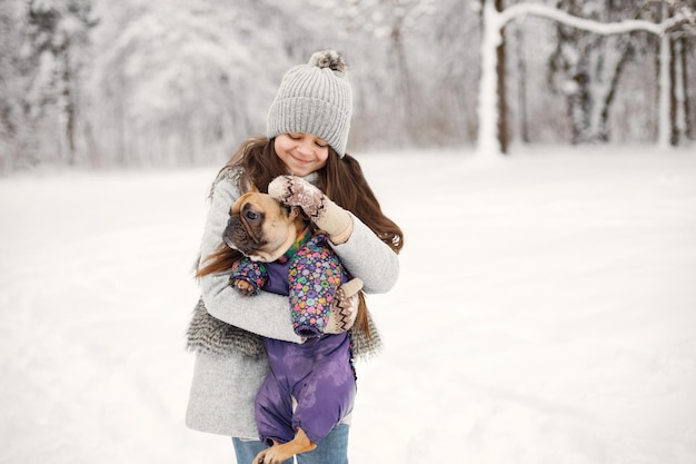 Mädchen in Strickmütze spielt mit ihrem Hund französische Bulldogge auf einem Schnee