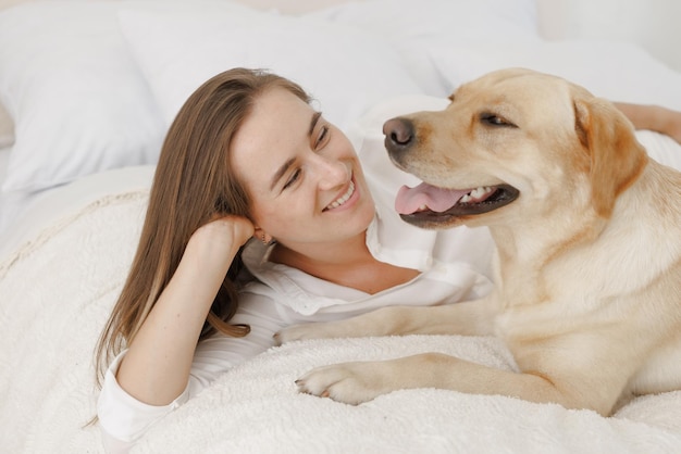 Mädchen in weißer Kleidung mit Hund Labrador, der zu Hause spielt