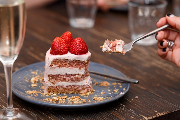 Mädchen isst einen süßen Kuchen mit Sommerbeeren auf einem Holztisch. Party, süßer Tisch. Sommer bieten Desserts im Restaurant.