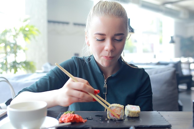 Mädchen isst Sushi und Brötchen in einem Restaurant / orientalische Küche, japanisches Essen, junges Modell in einem Restaurant