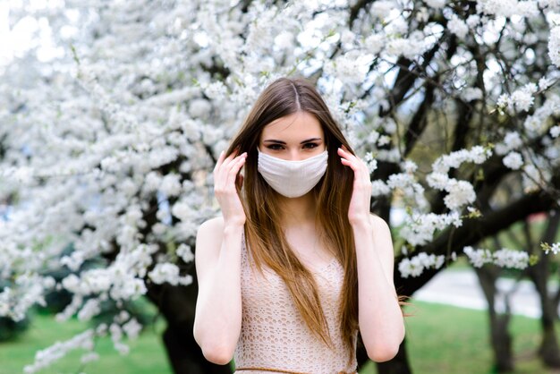 Mädchen, junge Frau in einer sterilen medizinischen Schutzmaske auf ihrem Gesicht im Frühlingsgarten. Luftverschmutzung, Virus, Pandemie Coronavirus-Konzept.