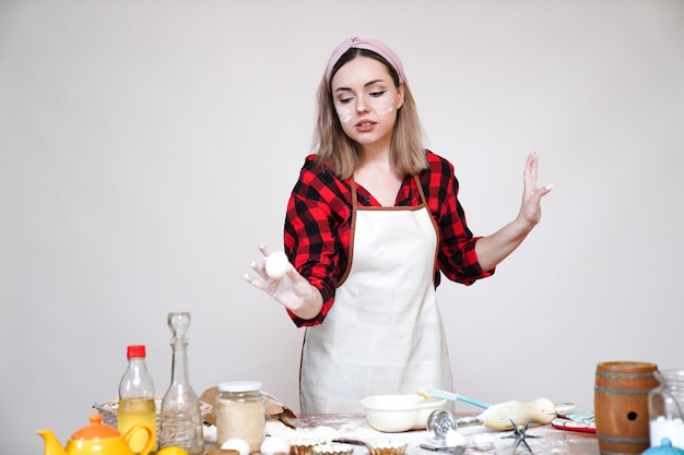 Mädchen kocht, Mädchen in der Schürze, Mädchen lustig mit Mehl befleckt, Mädchen, das Eier in der Hand hält