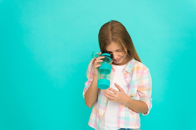 Mädchen kümmert sich um Gesundheit und Wasserhaushalt Kid halten Flasche blauen Hintergrund Langes Haar des Kindmädchens hat Wasserflasche Wasserhaushaltskonzept Gesund und hydratisiert Pädiatrische Störungen des Wasserhaushalts