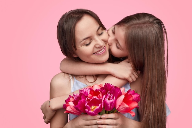 Mädchen küsst Mutter mit Frühlingsblumenstrauß