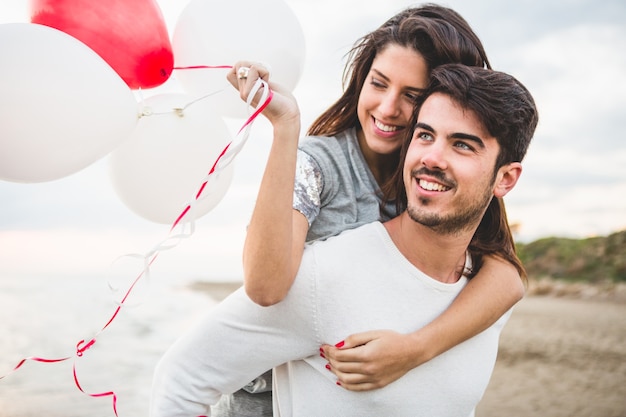 Foto mädchen lächelnd mit luftballons, während ihr freund sie auf ihrem rücken trägt