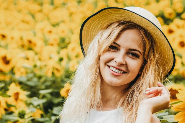 Mädchen lächelt und hält einen Hut. Im Hintergrund ist ein Sonnenblumenfeld zu sehen.