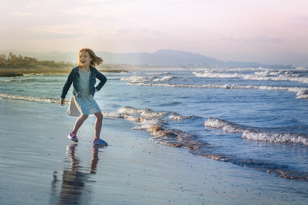 Mädchen läuft beim Spiel am Strand gegen den Himmel bei Sonnenuntergang