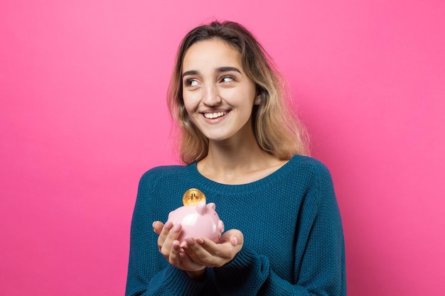 Mädchen legt in das Sparschwein physische BitcoinYoung Mädchen über rosa Hintergrund mit Sparschwein