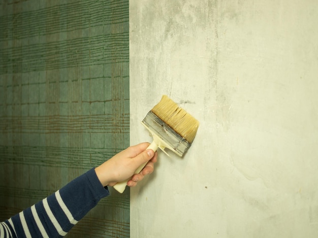 Mädchen legt Klebstoff auf die Wand für die Wandtapetierung Renovierung in der Wohnung