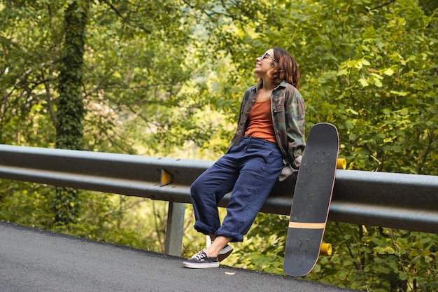 Mädchen lehnt am Zaun neben Skateboard