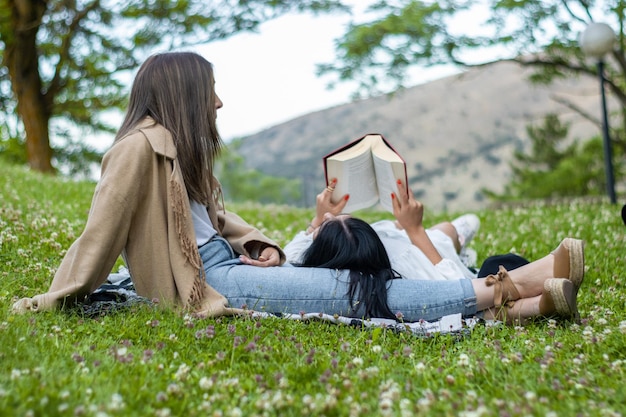 Mädchen liegt auf den Beinen ihres Freundes, während sie ein Buch auf dem Gras liest