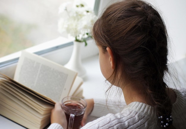 Mädchen liest Buch neben Fenster