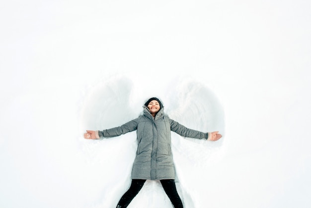 Mädchen macht einen Schneeengel im weißen Schnee.