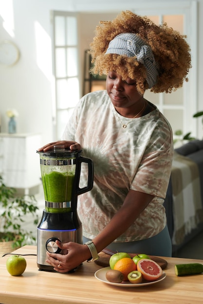 Mädchen macht grünen Smoothie im Mixer