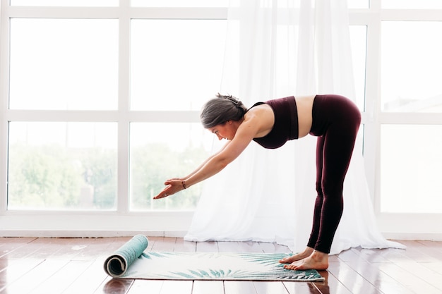 Mädchen macht übungen, stretching, yoga, in der nähe des fensters, yoga-anzug, körper, schlankheit und gesundheit, wir verteilen eine yogamatte, unterricht zu hause