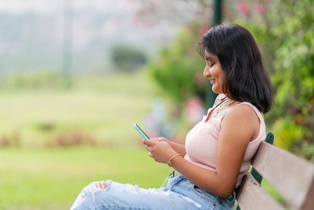 Mädchen mit andinen Gesichtszügen sitzt auf einer Parkbank und liest ihr Handy