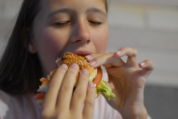 Mädchen mit Appetit isst einen leckeren Hamburger. Kind beißt ein großes Stück Sandwich ab