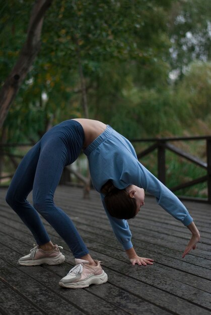 Foto mädchen mit athletischem körper im blauen turnanzug macht übungen bei bewölktem wetter im parkxd