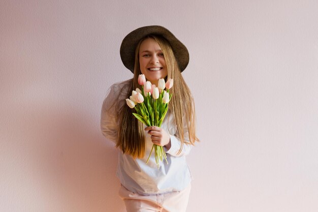 Mädchen mit blondem, langem, lockerem Haar hält Frühlingsblumen in den Händen