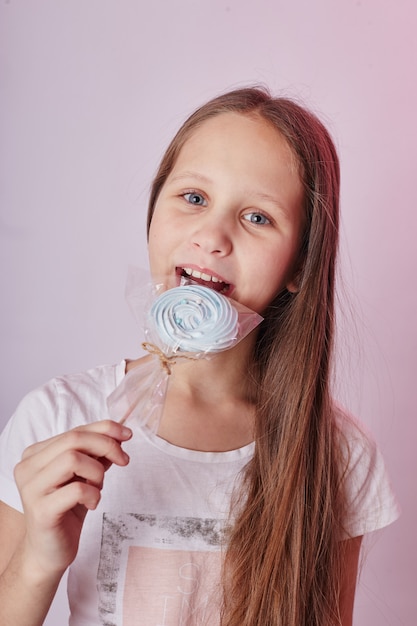 Mädchen mit blonden Haaren isst einen Lutscher, rundes Karamell am Stiel in den Händen eines fröhlich lächelnden Mädchens