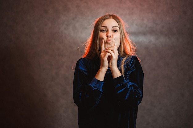 Mädchen mit blonden Haaren posiert emotional auf grauem Hintergrund. Ihr Haar ist rot erleuchtet