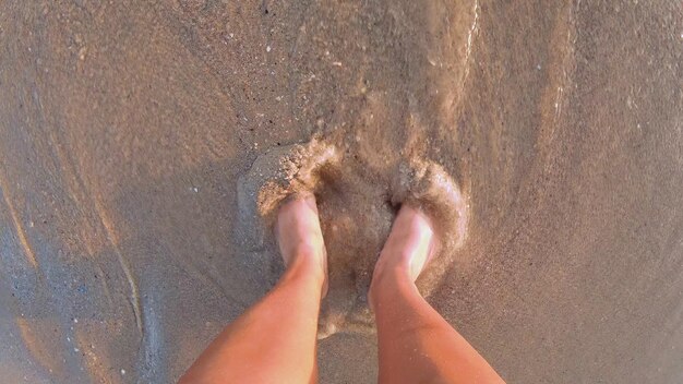 Mädchen mit bloßen und nackten Füßen, die bei Sonnenuntergang in den nassen Sand des Strandes an der Küste graben