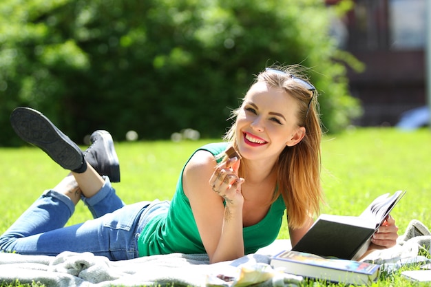 Mädchen mit Brille, die ein Buch in einem Sommerpark auf dem Gras liest.