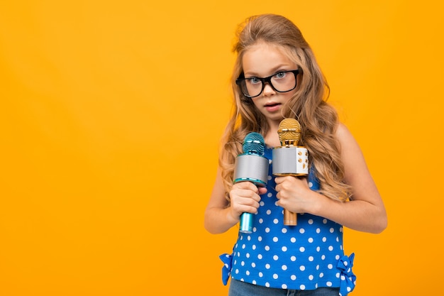 Mädchen mit Brille hält zwei Mikrofone an einer orangefarbenen Wand