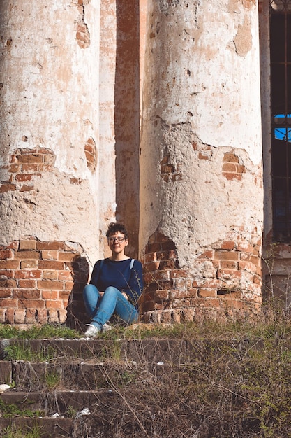 Mädchen mit Brille sitzt vor dem Hintergrund eines verlassenen Gebäudes und einer verlassenen Kirche