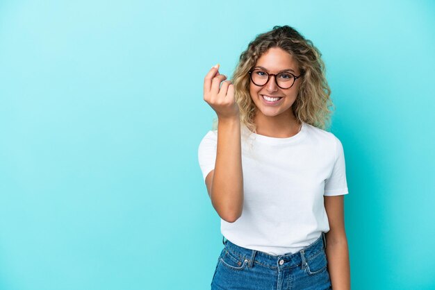 Mädchen mit dem lockigen Haar auf blauem Hintergrund isoliert, das Geldgeste macht